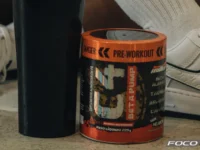 Close-up de suplementos de fitness e coqueteleira com uma pessoa sentada em roupa de ginástica