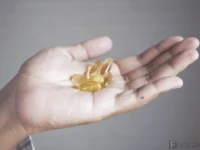 Uma mão segurando cápsulas de Ômega 3, representando suplementos e cuidados com a saúde.